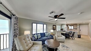 A modern living room with a sofa, armchair, and coffee table, a dining area with chairs, and a kitchen in the background.