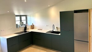 Eine moderne Küche mit dunklen Schränken, einem Edelstahlkühlschrank und einem Fenster mit Tageslicht.