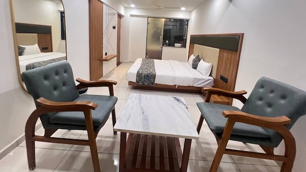 Une chambre d’hôtel de taille réduite, comprenant un lit, deux fauteuils, une petite table et un miroir.