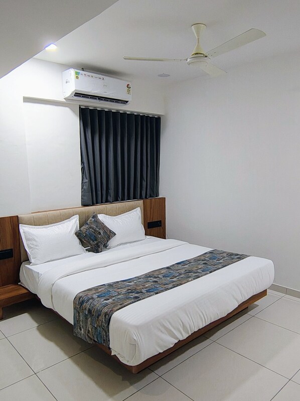 A bedroom with a bed, a ceiling fan, an air conditioning unit, and a window with curtains. - Hotel Royal Manor-Rajkot (Rajkot)