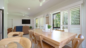 A dining area with a wooden table, chairs, and a TV mounted on the wall. - Liana One Coastal Mission Vibe (Mission Beach)