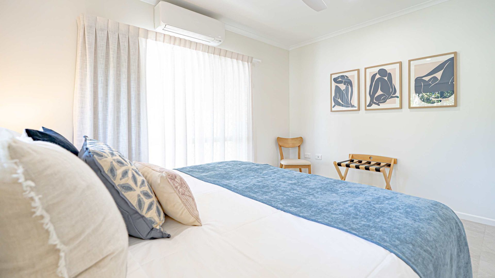 A bedroom with a bed, a chair, and three framed artworks on the wall.