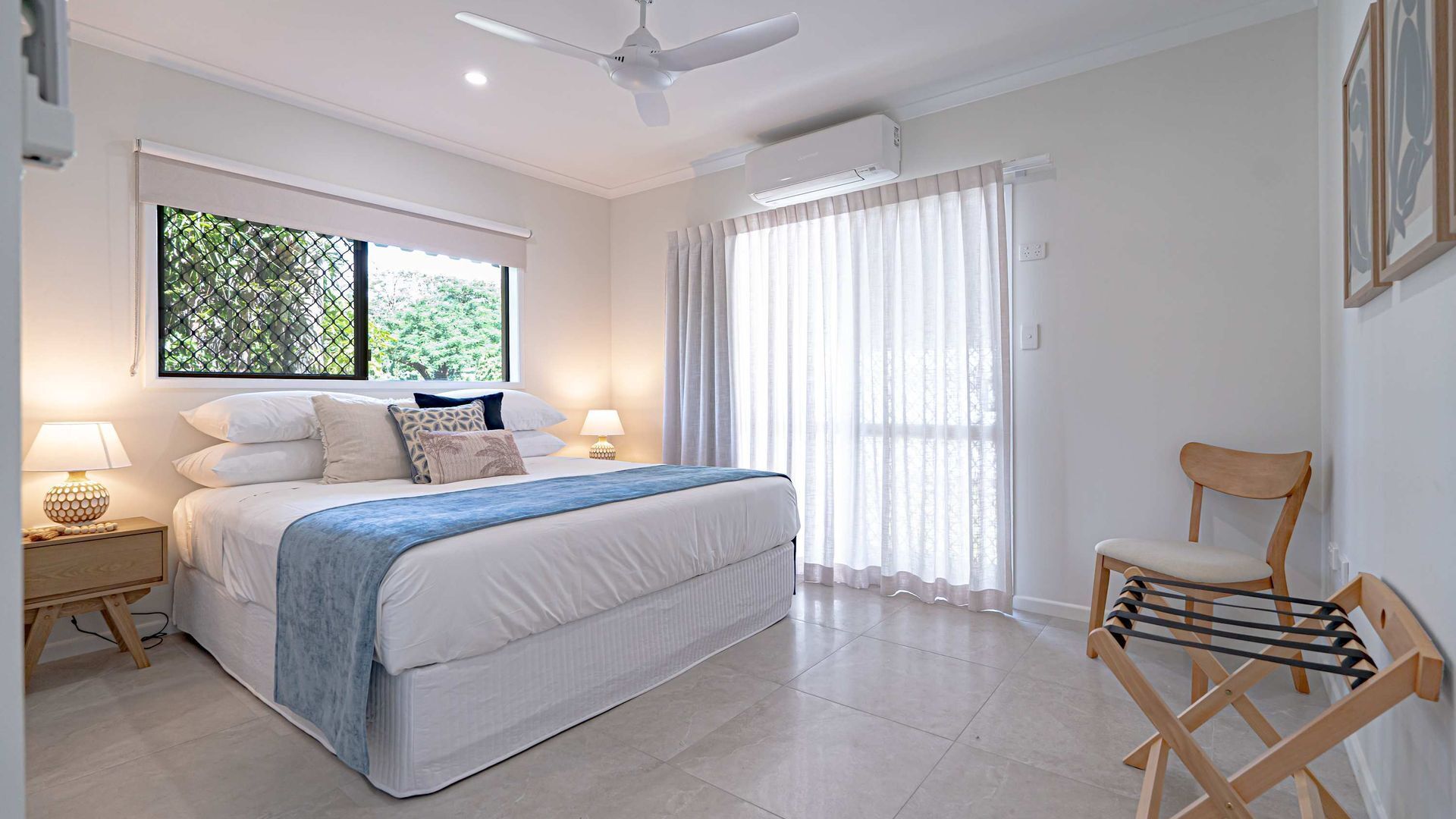 A bedroom with a bed, a chair, a nightstand, a window with curtains, and a ceiling fan.