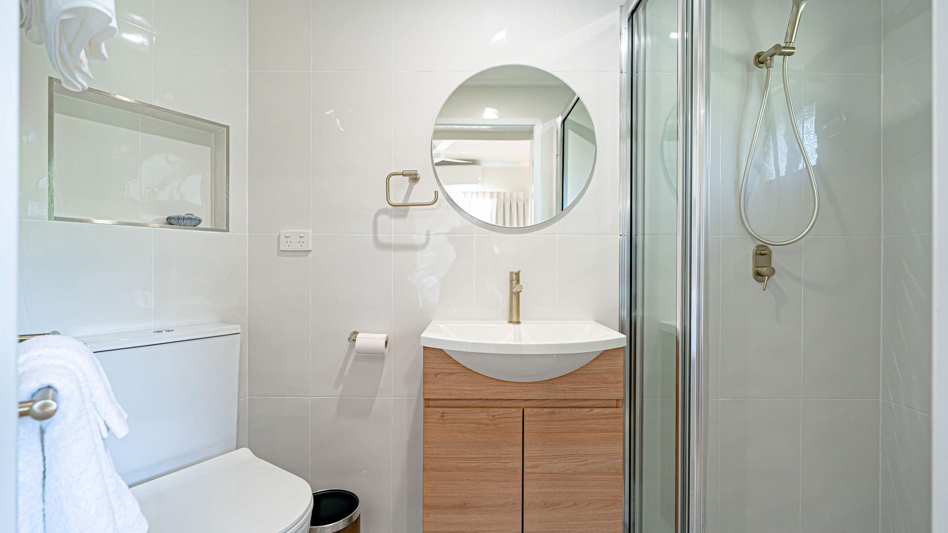Et moderne badeværelse med toilet, håndvask, spejl og glasbrusekabine.