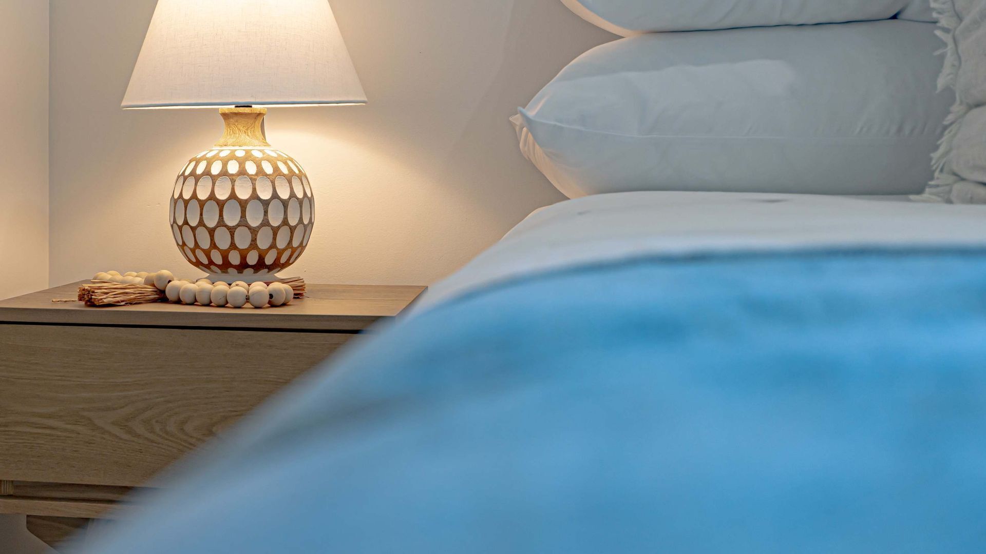 A bed with white bedding, a wooden nightstand with a patterned lamp, and a small decorative item on the nightstand.