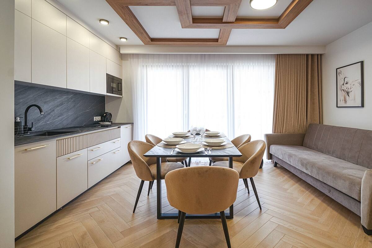 A modern kitchen with a dining table set for six, a sofa, and two framed artworks on the wall.