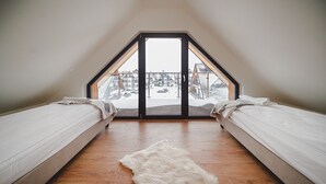 A bedroom with two beds, a wooden floor, and a view of a snowy landscape through a large window. - Resorts Sun&Snow Białka Tatrzańska P (Bialka Tatrzanska)