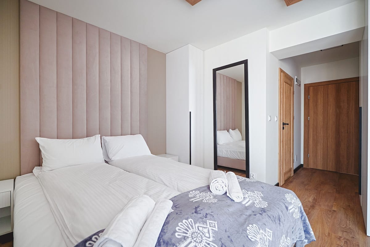 A modern hotel room with a large bed, a bedside table, a mirror, and a wooden door.