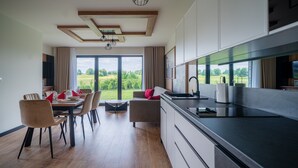 A modern kitchen with a large window, wooden flooring, and a dining area with chairs and a table set for two. - Resorts Sun&Snow Białka Tatrzańska P (Bialka Tatrzanska)