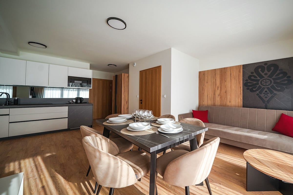 A modern living room with a dining area, wooden flooring, and a sofa with red cushions.