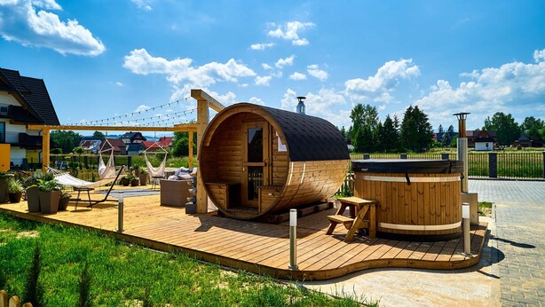 A wooden cabin with a curved roof, a hot tub, and a hammock on a wooden deck. - Resorts Sun&Snow Białka Tatrzańska P (Bialka Tatrzanska)