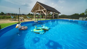 A swimming pool with inflatable toys, a wooden pavilion, and a grassy area with a hammock. - Resorts Sun&Snow Białka Tatrzańska P (Bialka Tatrzanska)