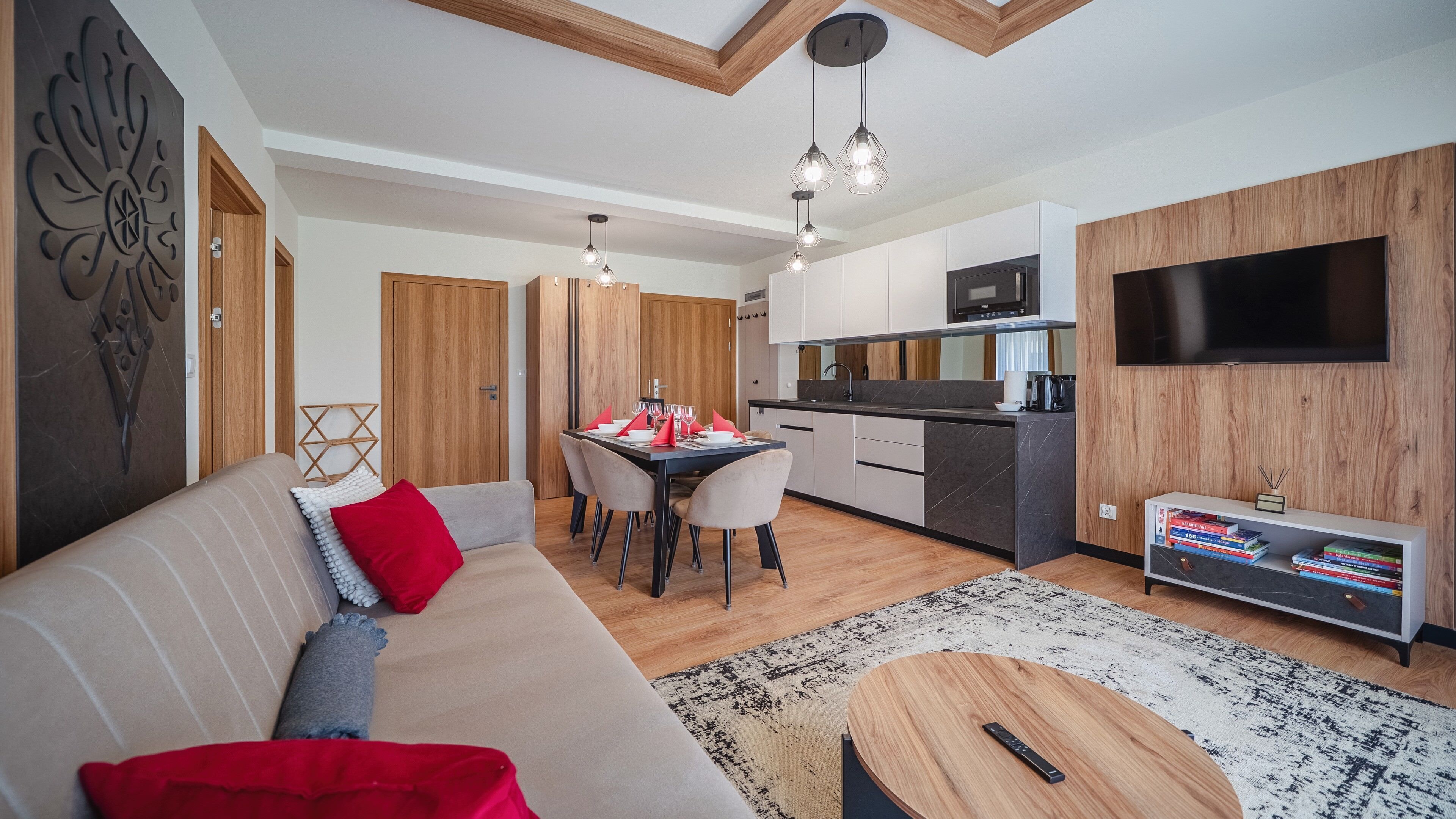 Uma sala de estar moderna com um sofá, um espaço de refeições com cadeiras, uma cozinha com micro-ondas e uma TV fixada na parede.