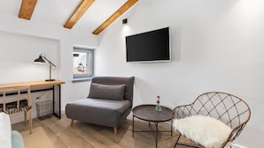 Una sala de estar moderna con un sofá, un sillón, una mesita, un escritorio y un televisor montado en la pared.