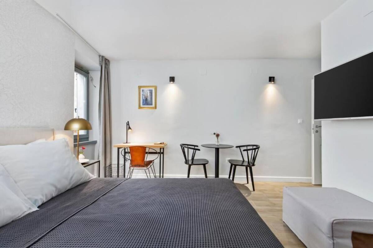 Una habitación de hotel moderna con una cama grande, un escritorio con dos sillas, una mesita con un florero y un cuadro en la pared.