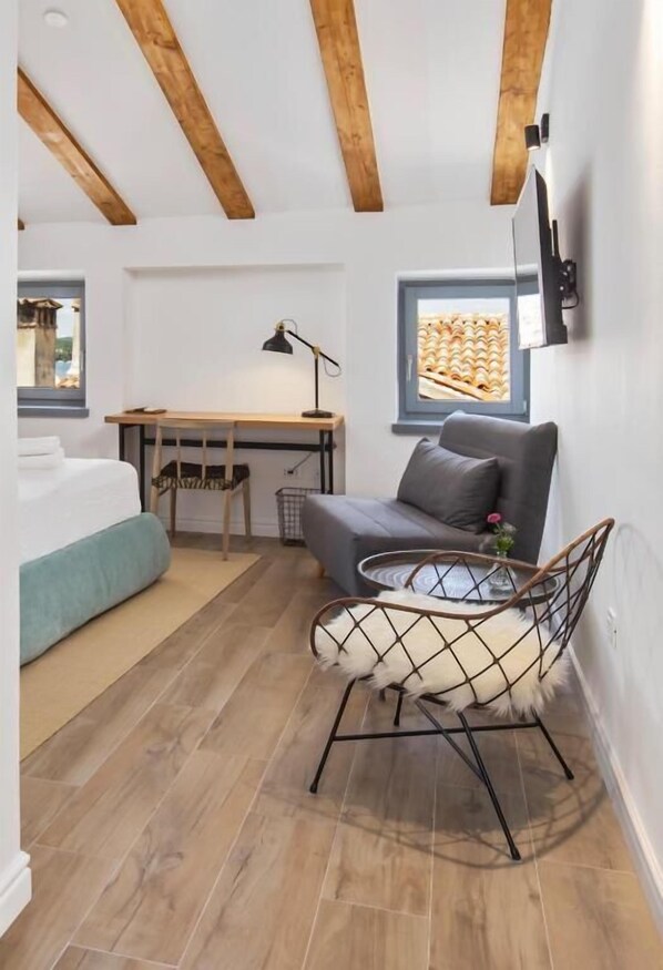 A compact room with a bed, a desk, a grey sofa, and a small round table.