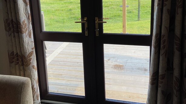 A room with a large sliding glass door leading to an outdoor area with a grassy field and a wooden deck.