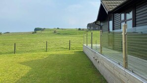 A building with a glass enclosure, a grassy field, and a hilly landscape in the background.
