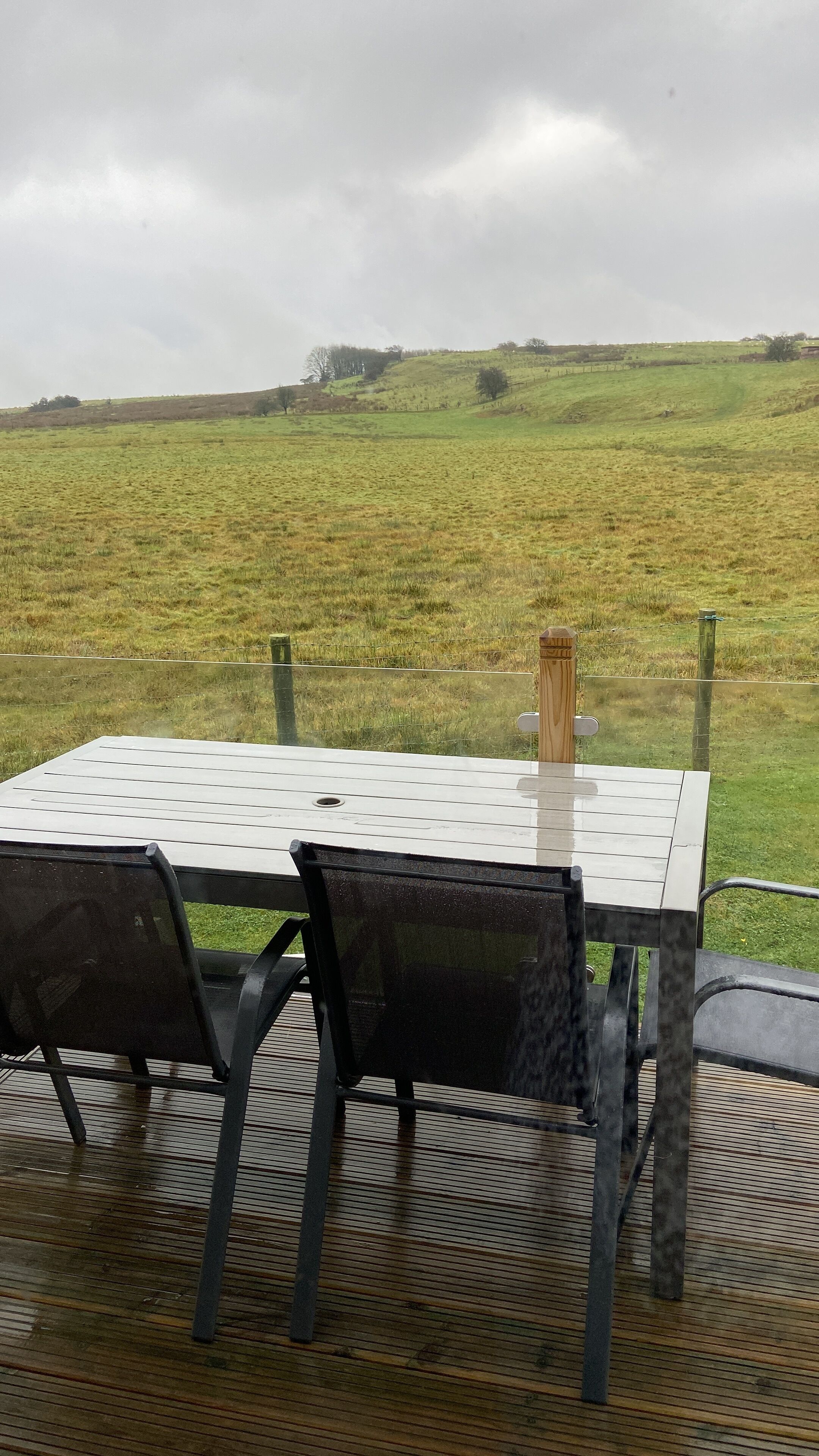 A table with chairs in a covered outdoor area, overlooking a grassy field.