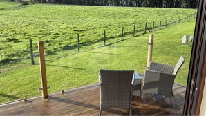 A deck with wicker chairs overlooking a grassy field with a fence.