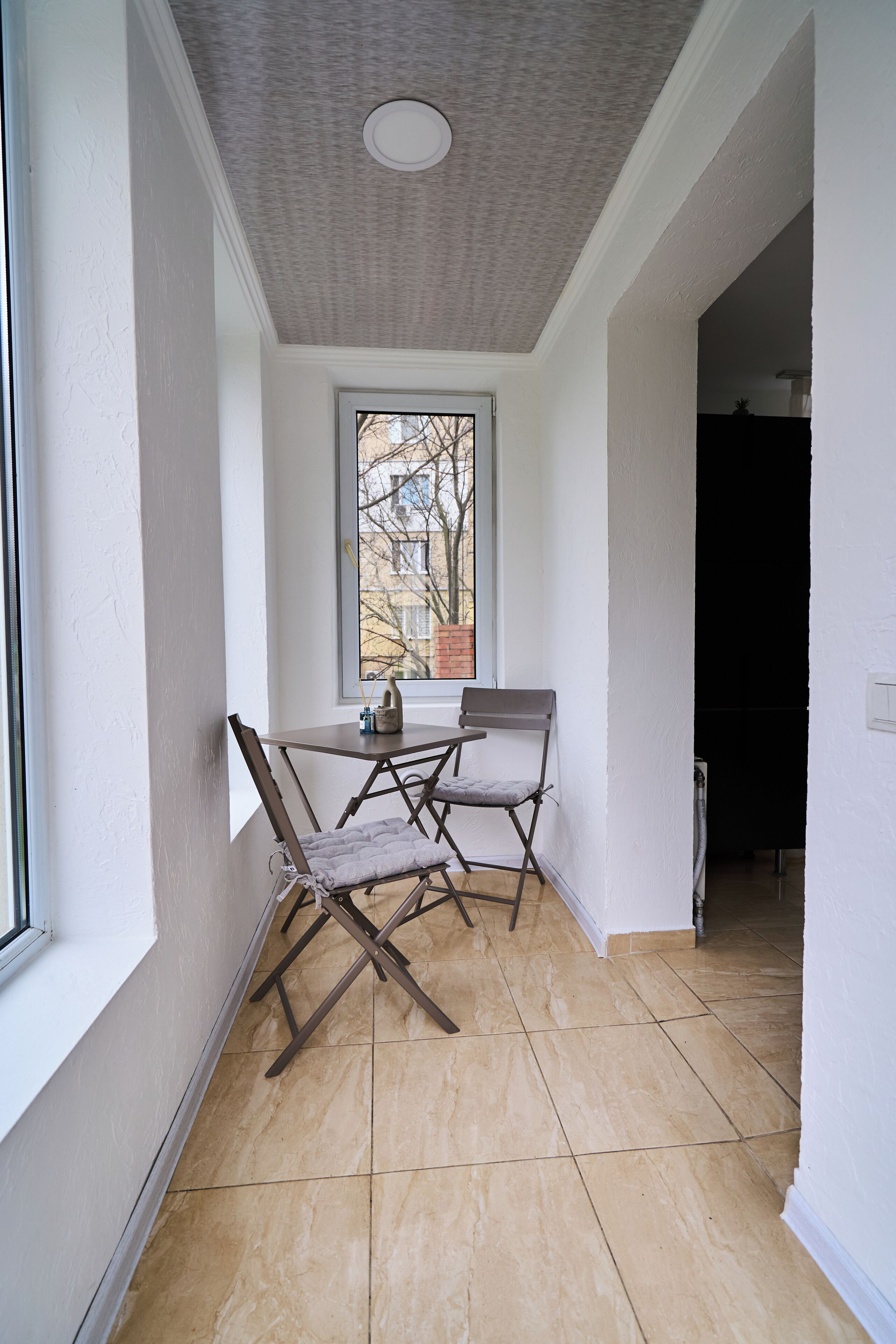 A narrow hallway with a window, a table with chairs, and a radiator.