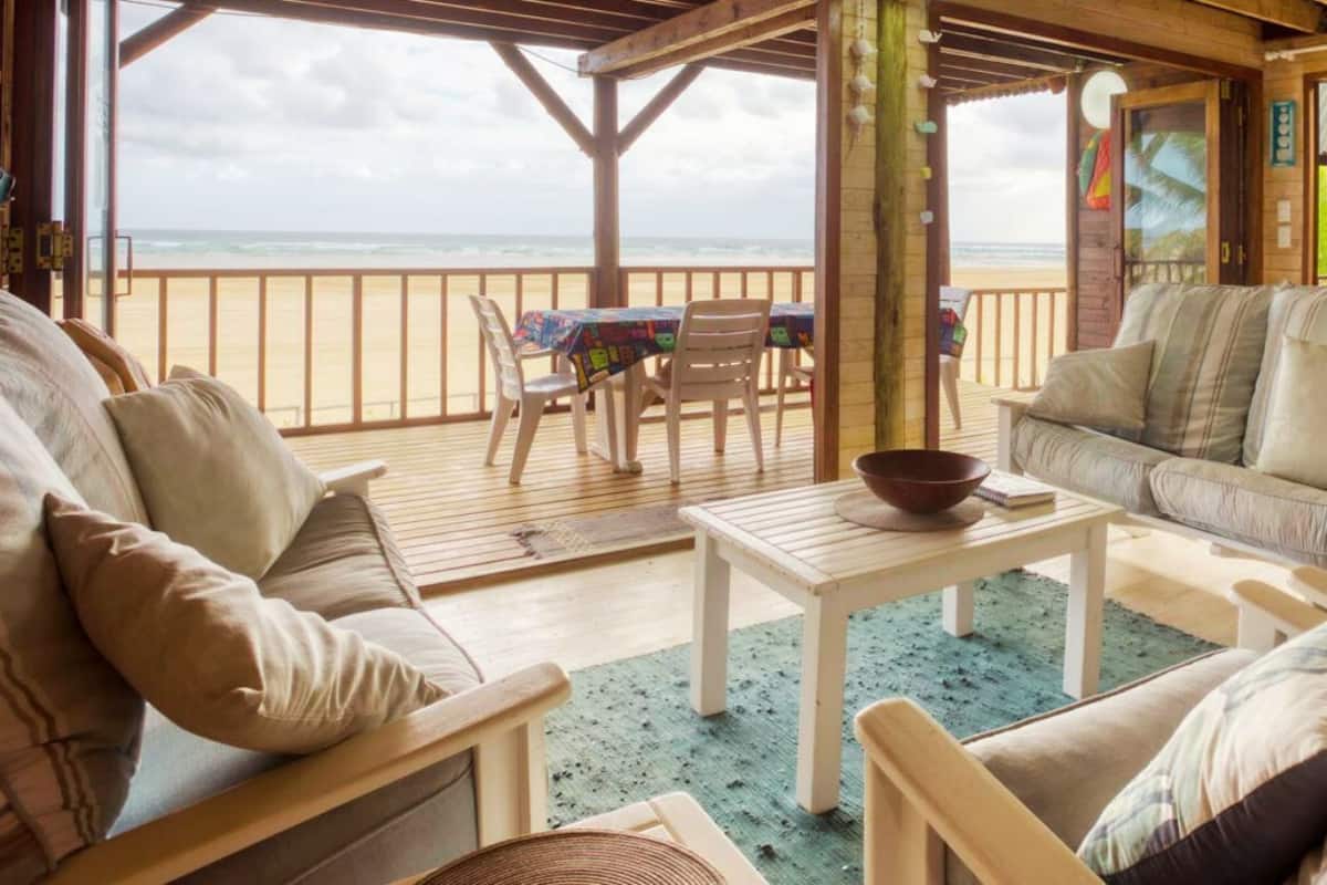 A cozy outdoor seating area with a view of the beach, wooden furniture, and a table with a bowl.
