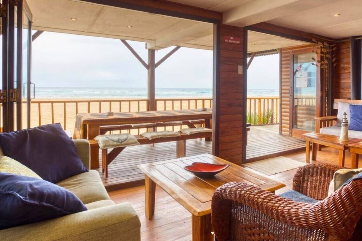 A cozy room with a wooden floor, a sofa, a dining table, and a view of the beach.