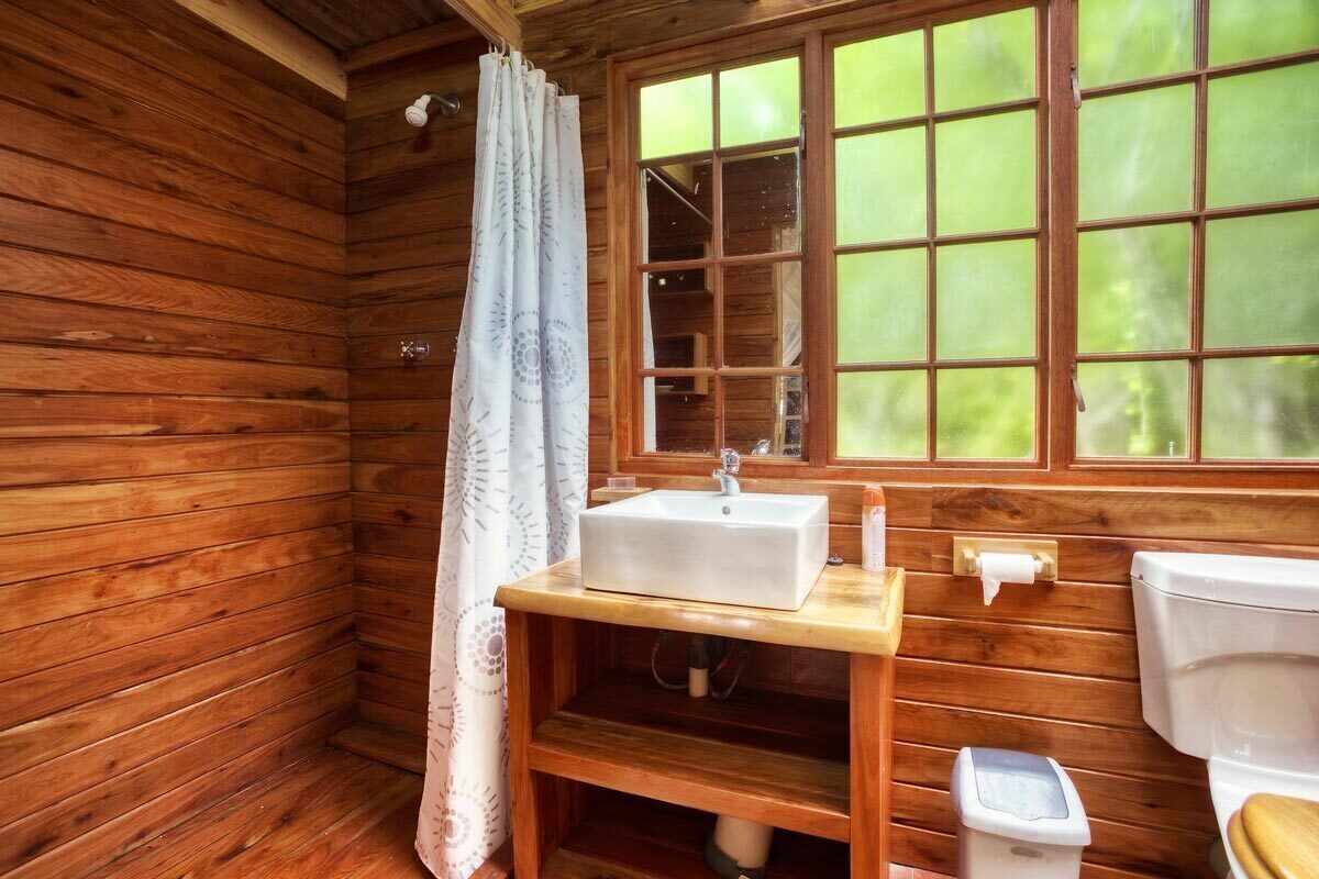 A wooden cabin bathroom with a window, a sink, a toilet, and a shower curtain.