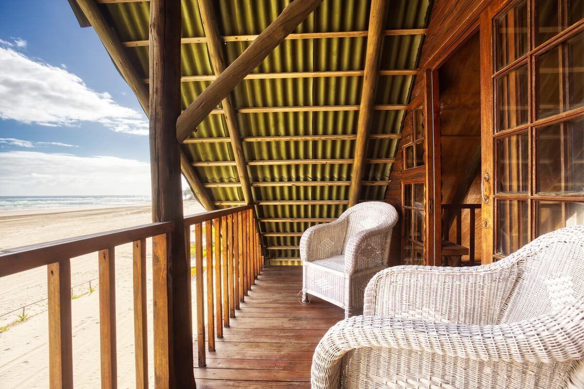 A covered porch with wicker furniture overlooking a beach.
