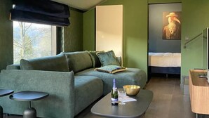A modern room with a green sofa, a small table with a bottle and bowl, a bed, and a painting on the wall. - House in Durbuy Near Town Center (Durbuy)