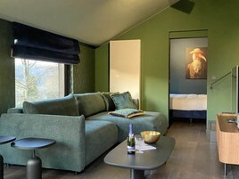 Una habitación moderna con un sofá verde, una mesita con una botella y un cuenco, una cama y un cuadro en la pared.