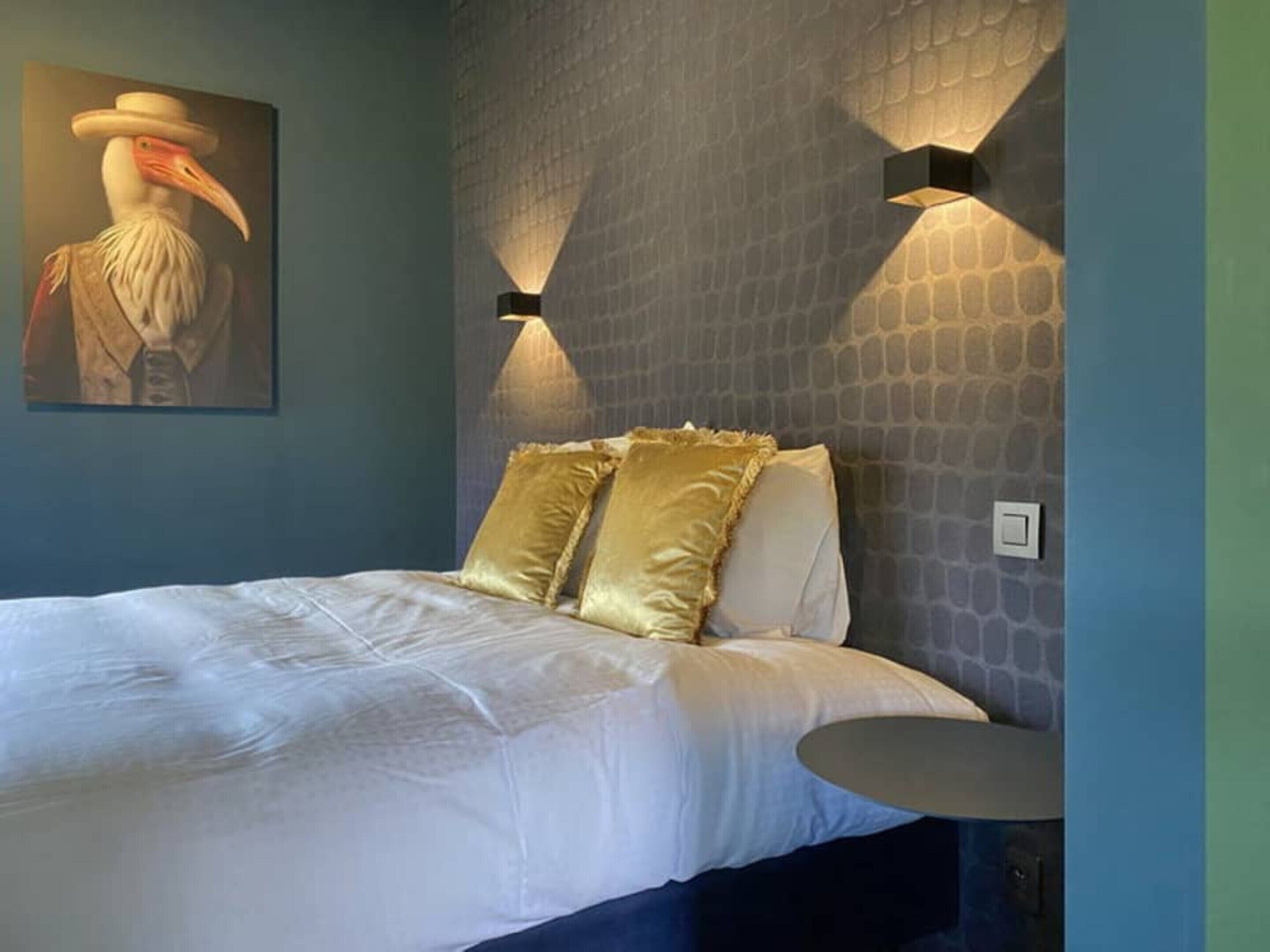Une chambre à coucher avec un lit, un luminaire fixé au mur et un tableau.