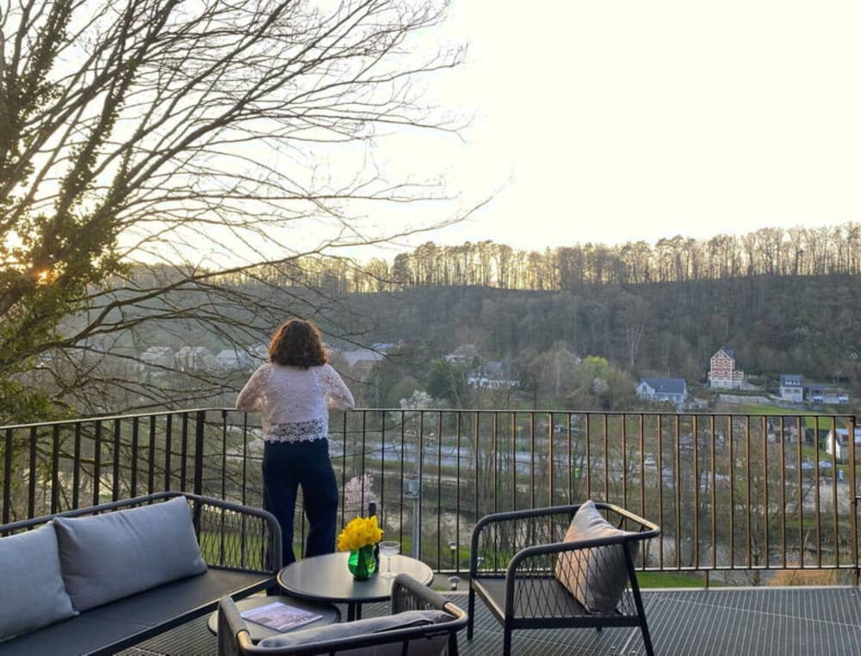 Un balcon donnant sur une zone boisée et un bâtiment situé au loin.