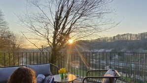 A balcony with a sofa and chairs, overlooking a scenic landscape with trees and a distant view. - House in Durbuy Near Town Center (Durbuy)