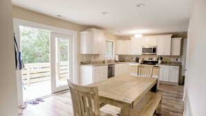 Une cuisine spacieuse avec des meubles blancs, une table en bois et une porte-fenêtre coulissante donnant sur un balcon.