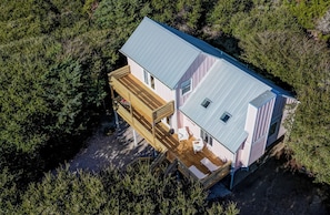 Een huis met twee verdiepingen, voorzien van een terras en een overdekte veranda, omgeven door dicht bos.