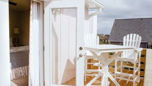 Une porte ouverte donnant sur un balcon où se trouvent une table en bois et deux chaises.