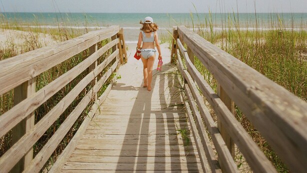 Une promenade en bois menant à une plage, avec un ciel dégagé.