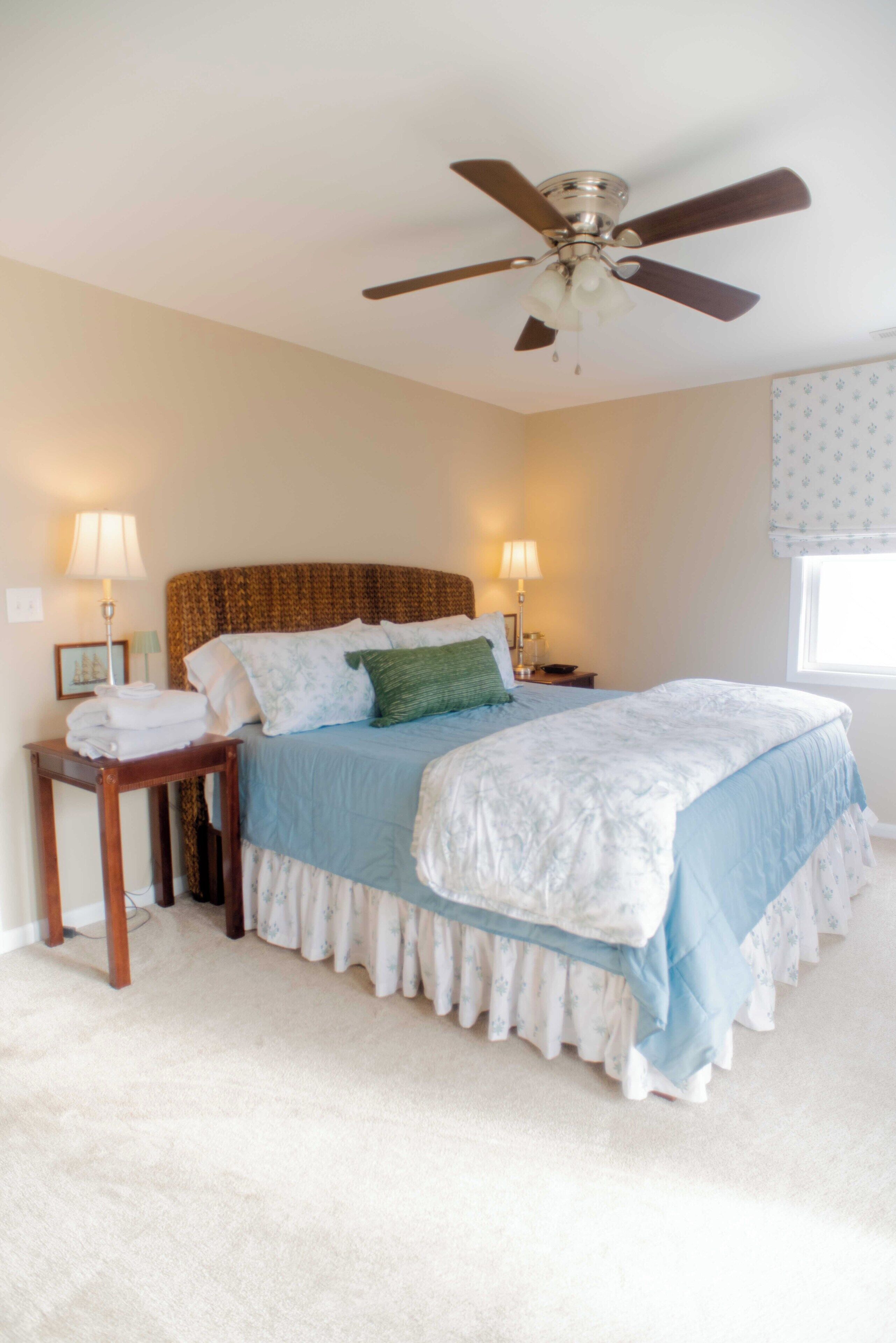 A bedroom with a bed, bedside tables, lamps, a ceiling fan, and a window with curtains.