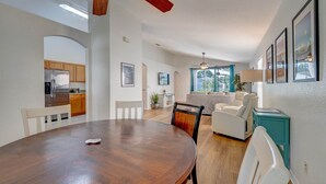 Una cocina moderna con electrodomésticos de acero inoxidable, un comedor con una mesa y sillas de madera, y una sala de estar con un sofá y una mesita auxiliar color aguamarina.