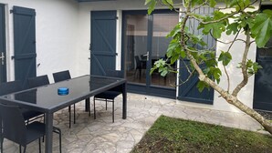 Eine Terrasse mit einem Glastisch und Stühlen, einem kleinen Baum und einem Ziegeldach.
