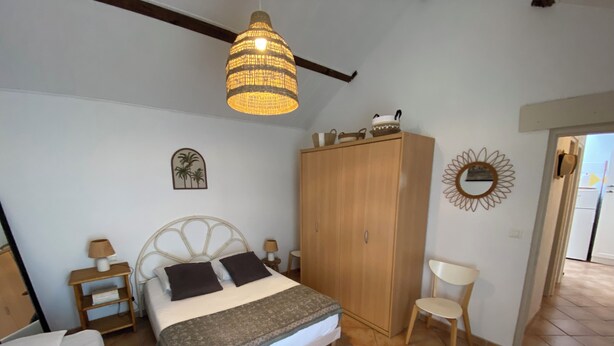 Ein Schlafzimmer mit Bett, Kleiderschrank, Stuhl, Lampe und einer Pendelleuchte.
