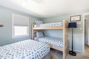 Quarto com duas beliches, janela com persianas, um certificado emoldurado na parede e um abajur.