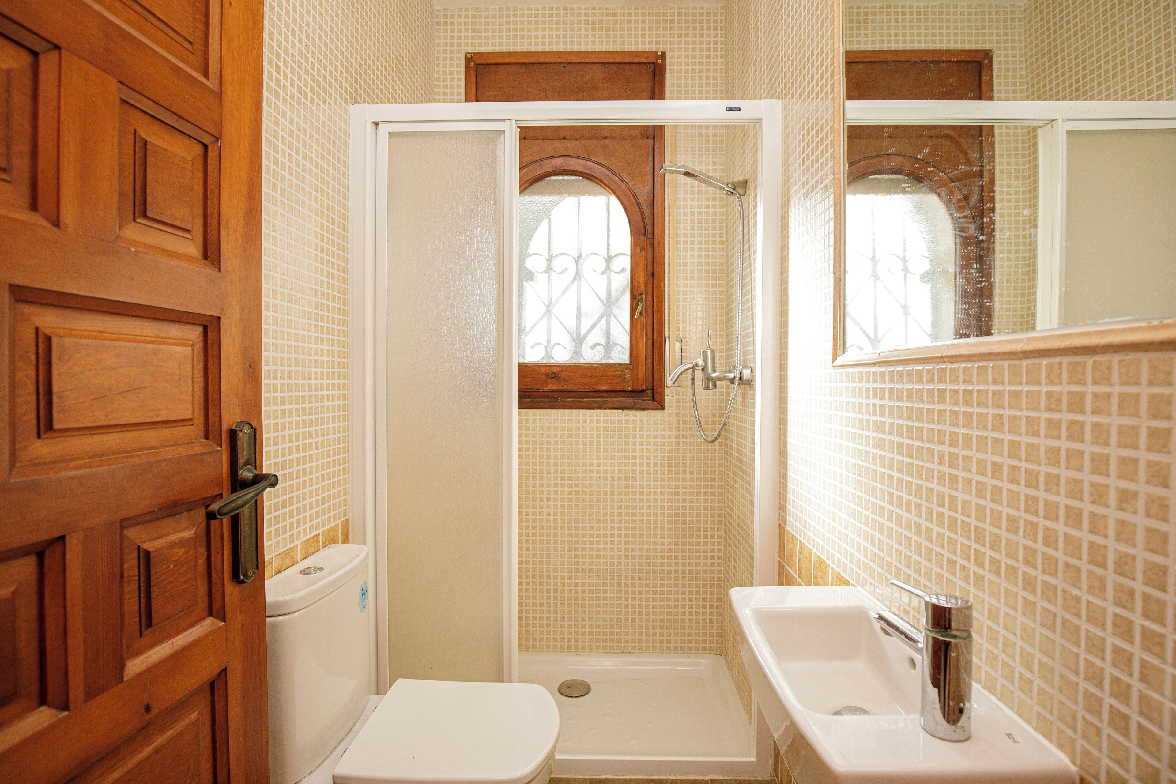 Een badkamer met een houten deur, een wit toilet, een douche met een glazen deur en een wastafel met een spiegel.