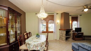 Ein Essbereich mit einer Kronleuchter, Holzsesseln, einem Tisch mit Blumenmuster-Tischdecke und einer Schrank mit Glastüren.