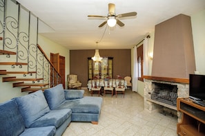 A living room with a blue sofa, a dining table with chairs, a fireplace, and a television on a wooden stand.