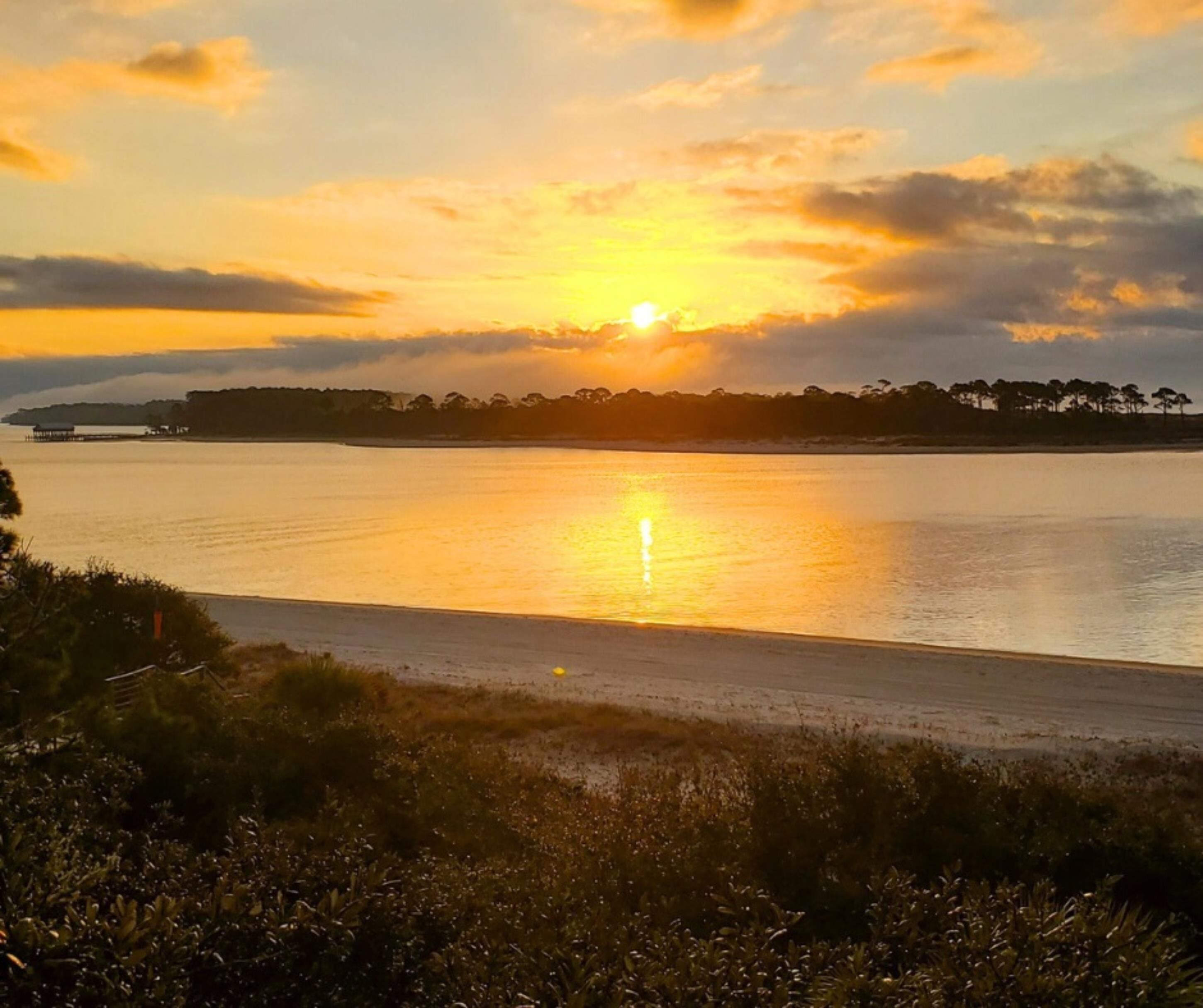 A sunset over a calm body of water with a distant shoreline and vegetation.