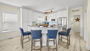 Een moderne keuken met witte kasten, een centraal eiland met barstoelen en een bord met de tekst 'WELCOME'.