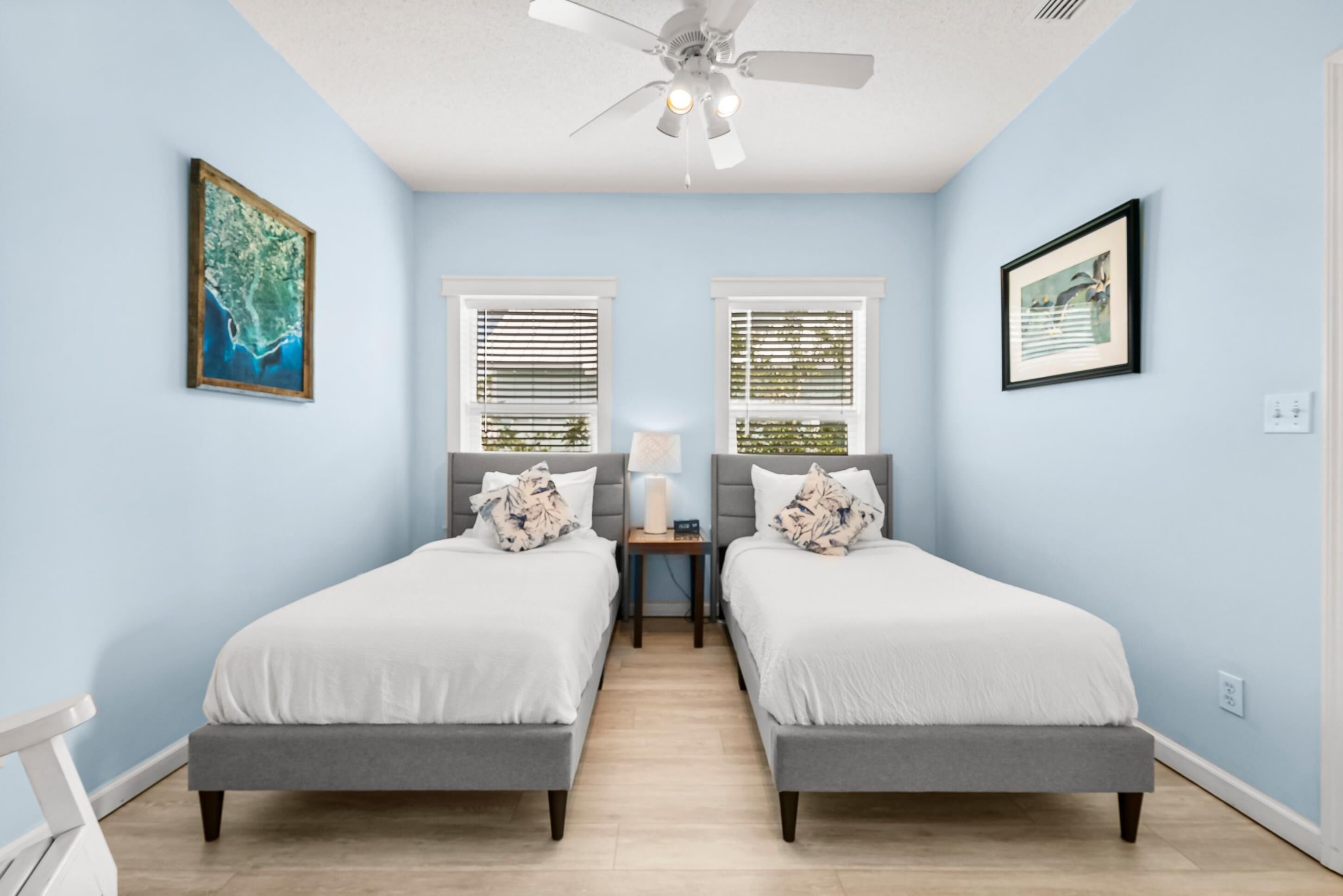 Un dormitorio con dos camas, un ventilador de techo y dos ventanas con persianas.