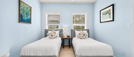 A bedroom with two beds, a ceiling fan, and two windows with blinds.